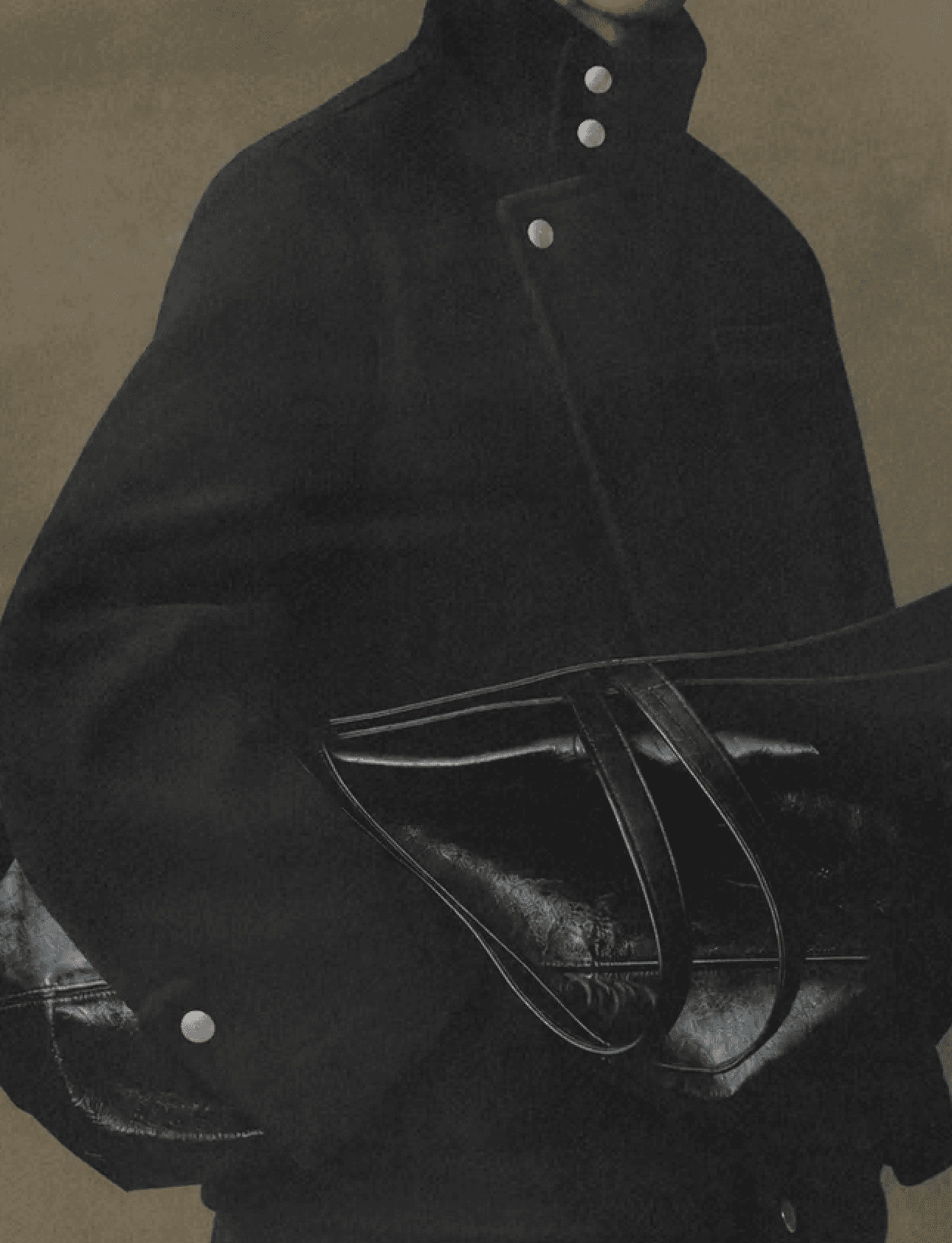 Close up of a black R/K2 wool jacket with silver snaps and a black leather bag under the arm