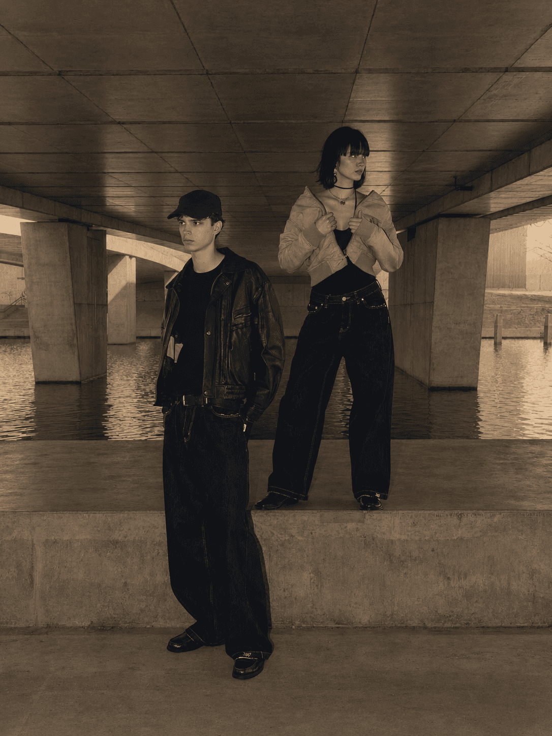 Two figures in wide R/K2 denim under a concrete bridge